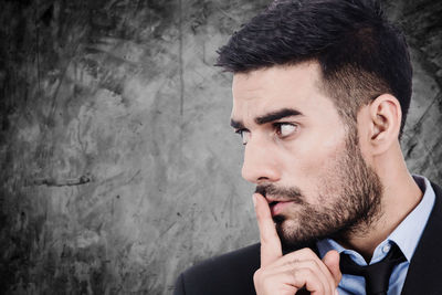 Close-up of businessman with finger on lips looking away against wall