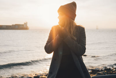 Woman standing by sea against sky during sunset