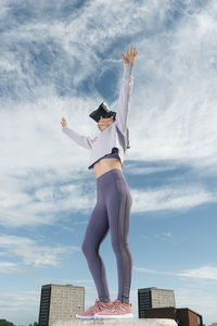 Woman outside wearing virtual reality headset with her arms outstretched, urban backdrop.