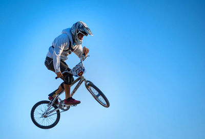 Full length of man in mid-air performing stunt on bicycle against clear blue sky