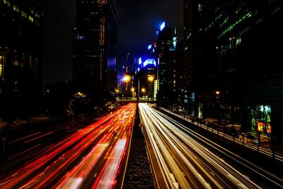 High angle view of light trails over street amidst buildings in city at night