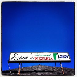 Low angle view of sign board against clear blue sky