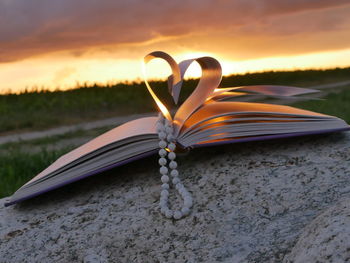 Book pages with beads necklace making heart shape on rock at sunset