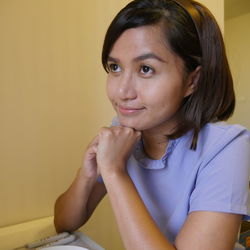 Thoughtful woman with hands on chin sitting by yellow wall