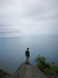 Man looking at sea against cloudy sky