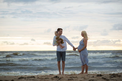 Man with daughter holding pregnant woman hand at beach