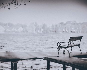 Empty bench by river against clear sky during winter