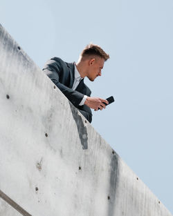 Side view of young man using mobile phone against sky