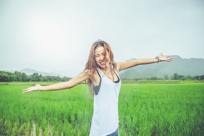 Young woman with arms raised on field against sky