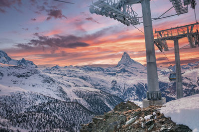 Cable cars moving by matterhorn mountain against cloudy sky during sunset