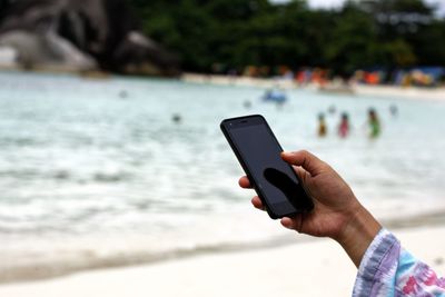 Close-up of hand holding mobile phone at beach