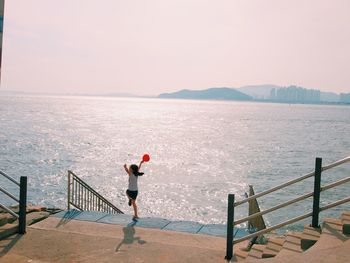 Man standing on railing by sea against sky