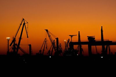 Silhouette cranes at against clear orange sky during sunset