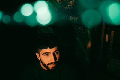 Young beard man looking away under illuminated green lights at restaurant