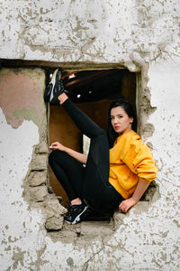 Portrait of beautiful young woman sitting on window against wall