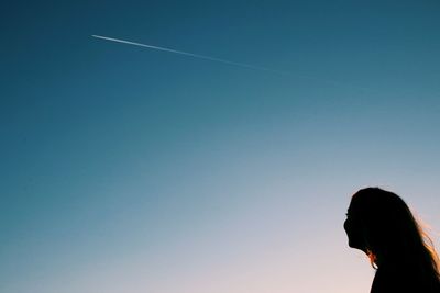 Silhouette woman looking at vapor trail against clear blue sky
