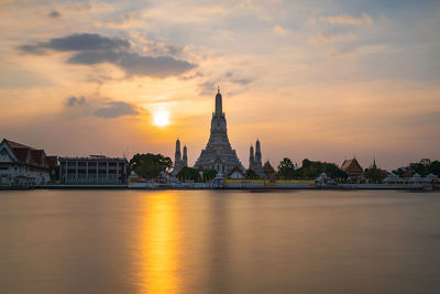 Scenic view of river by buildings against sky during sunset