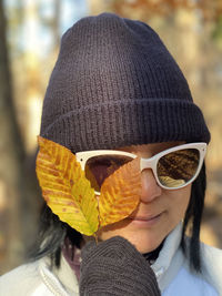 Close-up of woman wearing sunglasses holding autumn leaves