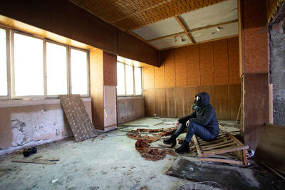 Side view of man sitting on chair in abandoned building