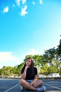 Portrait of young woman sitting on road against sky