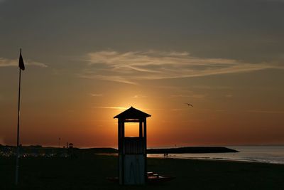 Silhouette beach by sea against sky during sunset