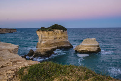 Rock formations at sea against sky during sunset 