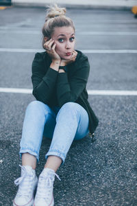 Portrait of young woman using mobile phone while sitting on road