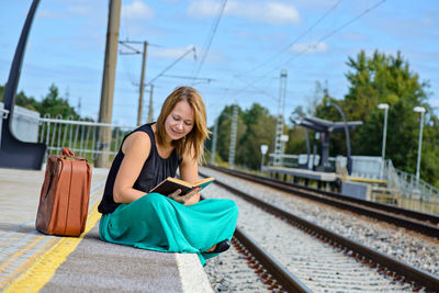 Young woman using phone while sitting on railroad platform