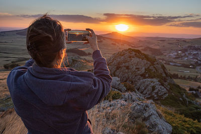 Person photographing a sunset over the reliefs of the haute loire in france