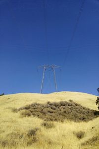 Low angle view of electricity pylon on field against blue sky