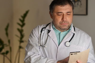 Close-up of mature doctor using phone against wall