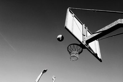 Low angle view of cropped hands playing basketball against clear sky