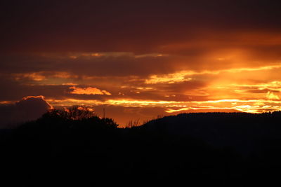 Silhouette landscape against dramatic sky during sunset