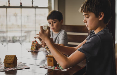 Two young boys decorating gingerbread houses together at the table.