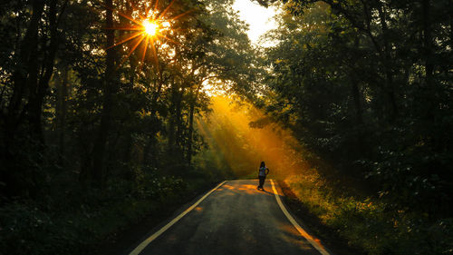 Woman standing on road amidst trees in forest