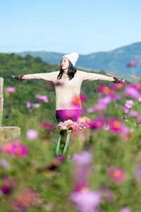 Woman standing with arms outstretched by flowering plants