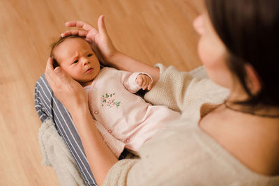 Cute small baby girl wear pajamas wake up lying on mother hand in bed in room closeup top view