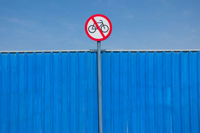 Low angle view of forbidden sign on blue wall against sky during sunny day