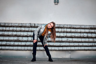 Full length portrait of young woman against wall