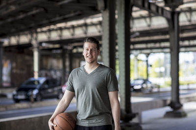 Portrait of young man with basketball standing on bridge