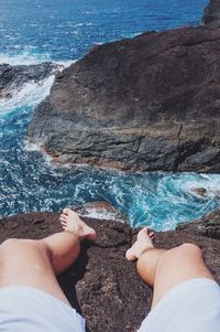 Low section of man sitting on cliff against sea