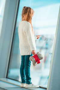 Side view of girl with stuffed toy standing by window