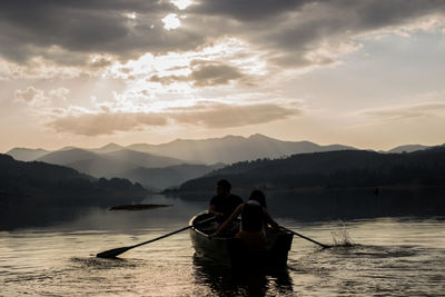 Rear view of men on boat in lake against sky during sunset