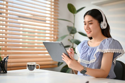 Young woman using digital tablet while sitting on table