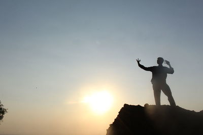 Silhouette man standing on rock against sky during sunset