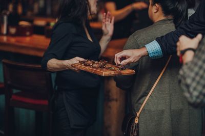 Midsection of woman serving appetizer to friends in party at home