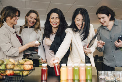 Smiling multi-ethnic businesswomen looking at juice bottles on table in event