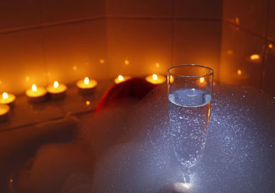Digital composite image of sparkling wine against illuminated tea lights in bathroom