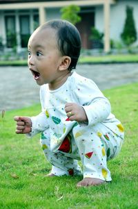 Cute baby girl shouting while crouching on grassy field