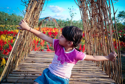 Full length of cute girl with arms raised on plant